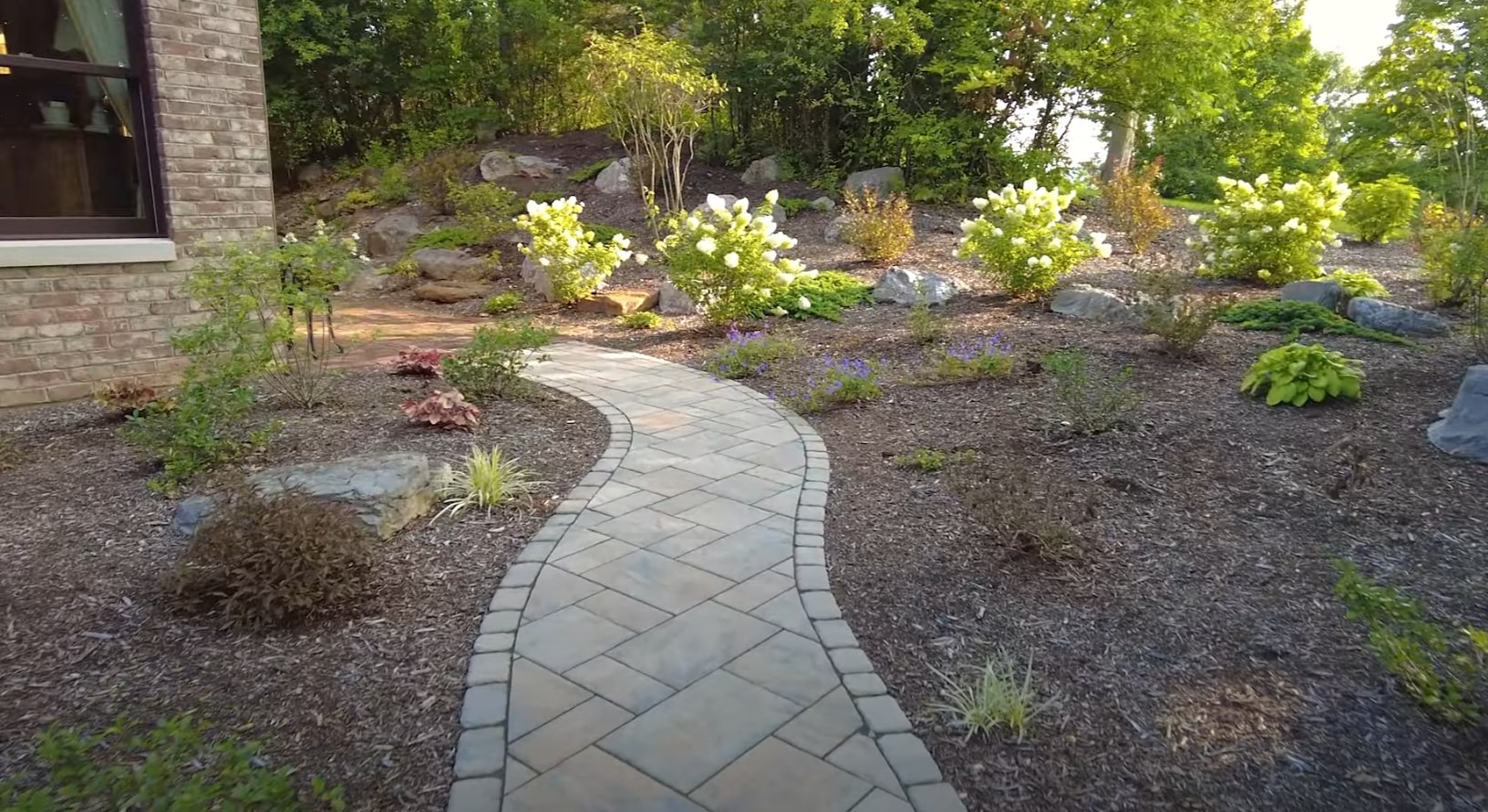 Custom hardscaping and pathway design services Beautiful stone pathway through landscaped garden with flowering plants